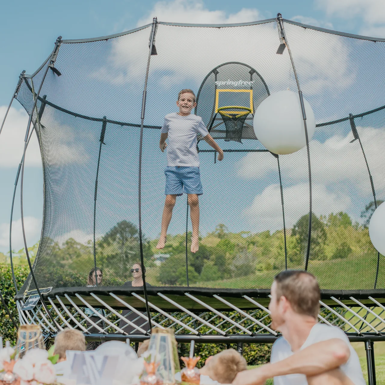 Dítě na trampolíně Springfree Large Square S113 při oslavě na zahradě