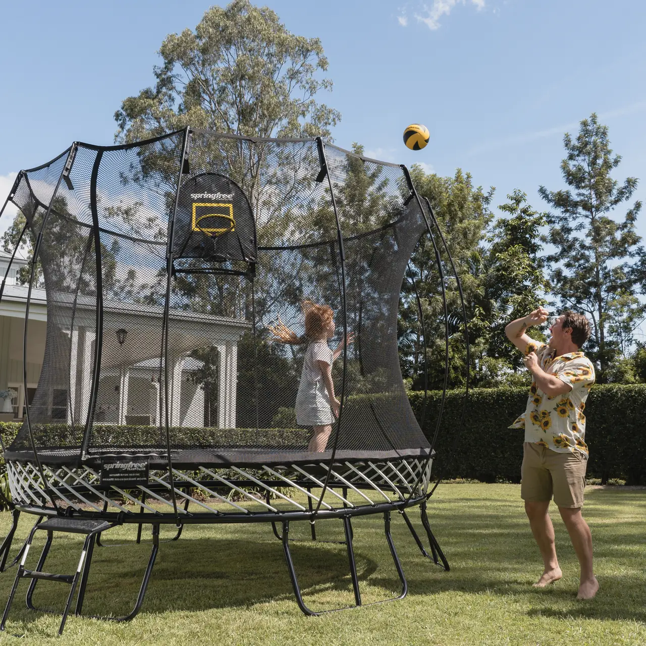 Děti hrají u trampolíny Springfree s košem FlexrHoop