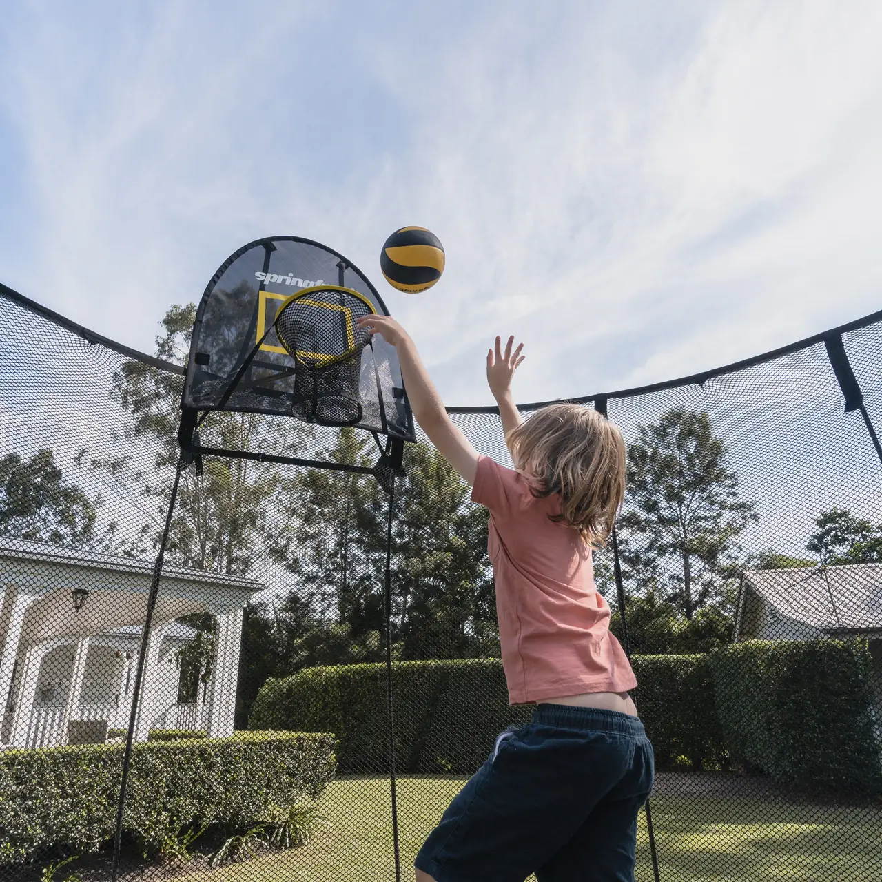 Dítě hází míč do koše FlexrHoop na trampolíně Springfree