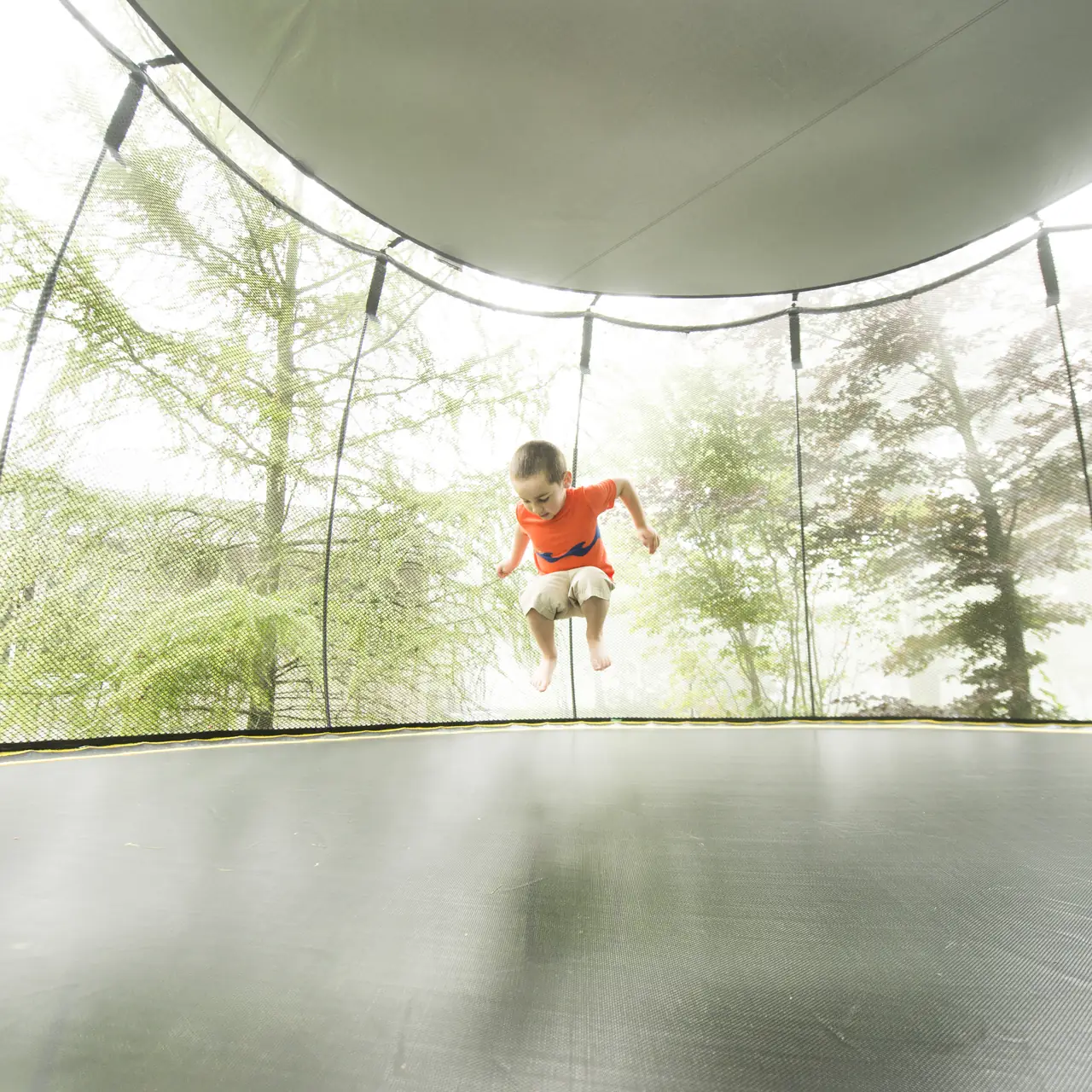 Dítě skáče na trampolíně Springfree pod sluneční clonou