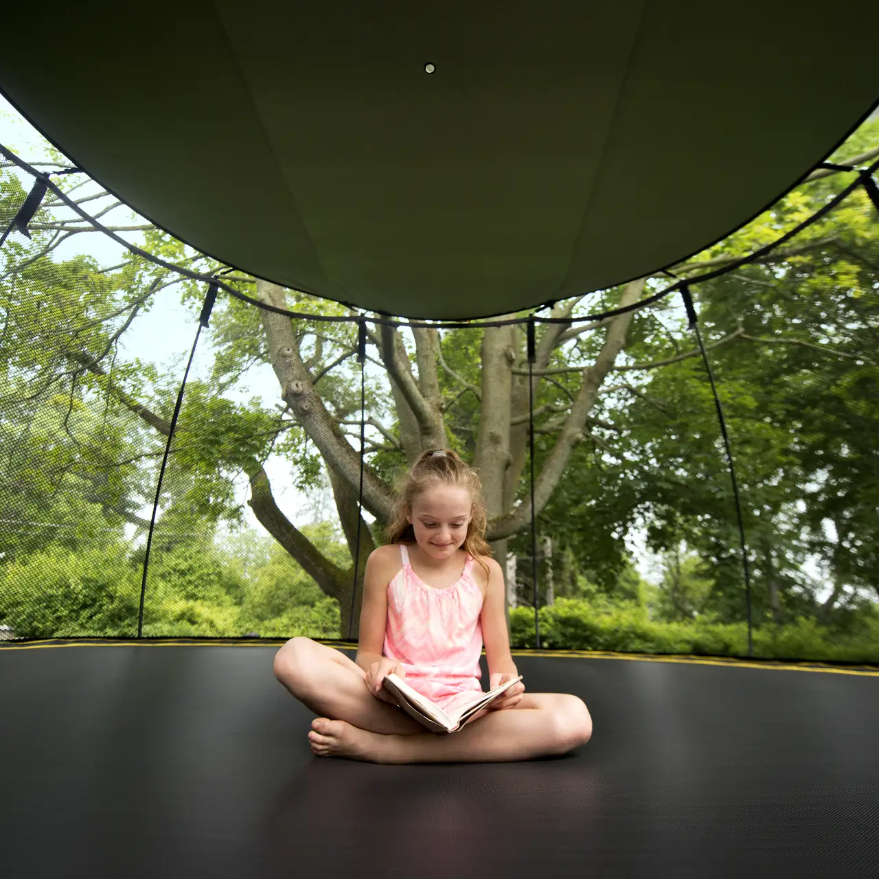 Dítě sedí na trampolíně Springfree pod sluneční clonou