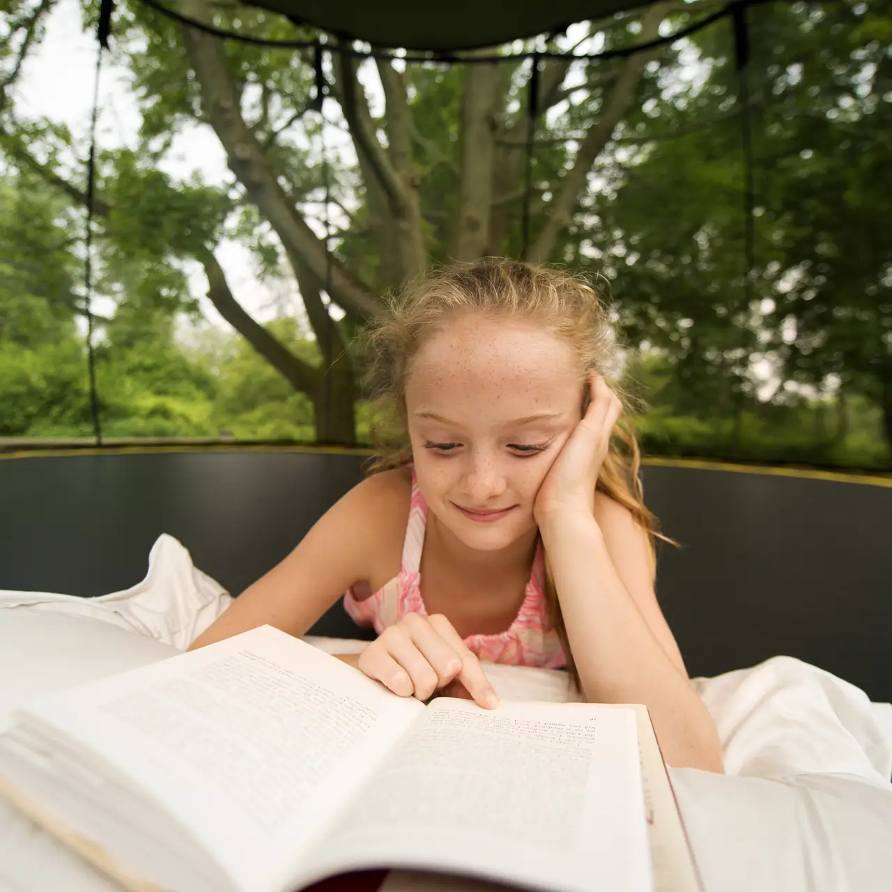 Dívka čte na trampolíně Springfree pod sluneční clonou