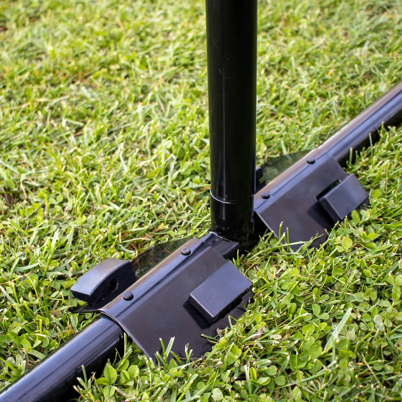 Detail kotvící sady Springfree v trávě u rámu trampolíny